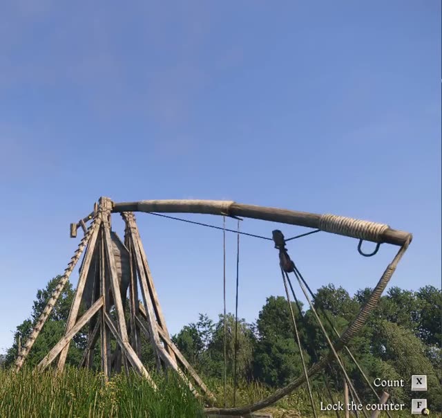 A wooden trebuchet standing in a field under a blue sky in Kingdoms Connected